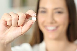 A blurred, smiling woman holding an oral dental sedative between her fingers